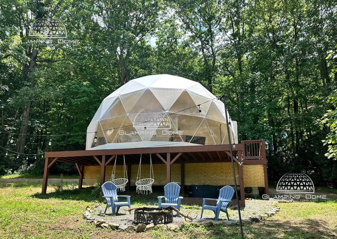 Exterior view of a 29.5-foot (9-meter) geodesic dome tent by Glamping Dome Store, ideal for outdoor setups. Elevated on a sturdy wooden platform with a front deck, the dome features a transparent window offering panoramic views. The area is adorned with string lights for a cozy ambiance. Beneath the platform are hanging chairs, and a fire pit with Adirondack chairs sits nearby. Nestled in a lush forest in Charlotte, North Carolina, USA, this semi-temporary structure is eco-friendly and unique.