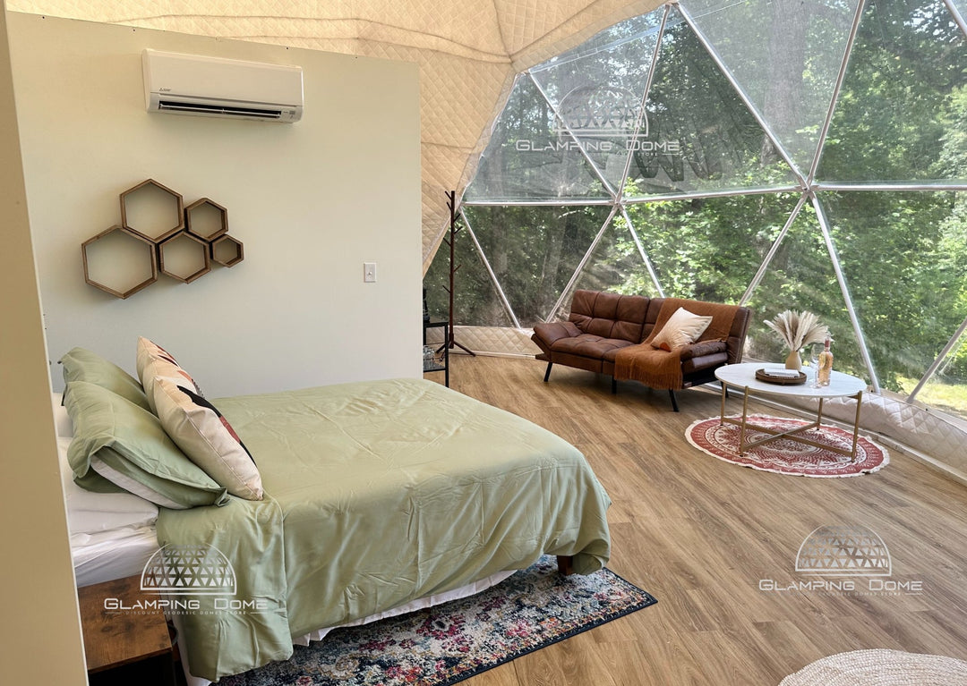 Interior of a 29.5-foot (9-meter) geodesic dome tent by Glamping Dome Store, located at Big Little Clouds in Charlotte, North Carolina, USA. This stylish dome features a cozy bedroom with a green bedspread, hexagonal wall decor, and modern furnishings. A lounge area with a sofa and table is framed by large panoramic window offering stunning forest views of North Carolina, USA. Ideal for glamping businesses, dome tent rentals, or unique outdoor accommodations, perfect for Airbnb or B&B setups.