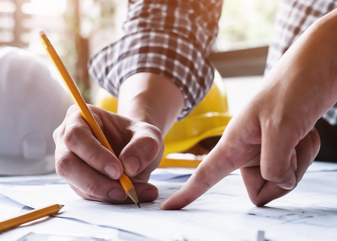 Close-up of engineers reviewing and marking up structural blueprints, symbolizing precision in engineering. A yellow hard hat in the background represents construction and safety. This image highlights the meticulous planning and professional structural assessment included in Glamping Dome Store’s Standard Structural Engineering Report, ensuring our geodesic dome tents meet wind and snow load requirements for safe and reliable installation.