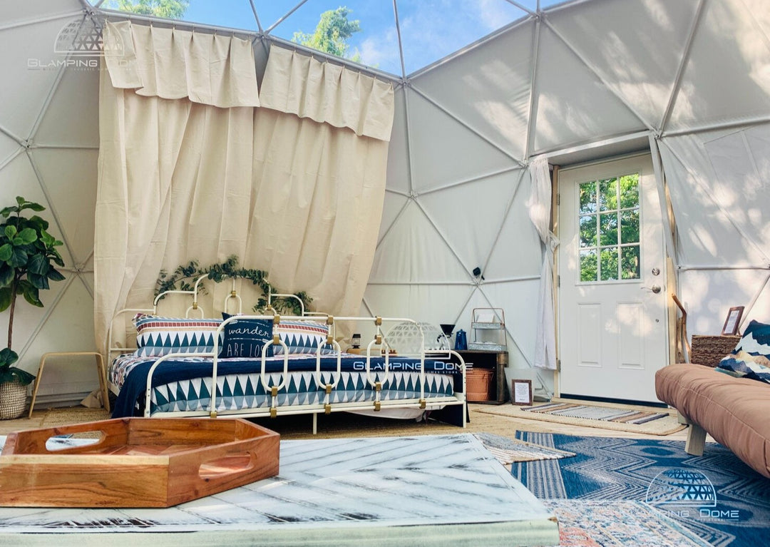 Interior view of a geodesic dome tent sold by Glamping Dome Store, measuring 19.7 feet (6 meters) in diameter, installed at Tiny Haven Living near Harpers Ferry, West Virginia, USA. This off-grid glamping dome features a cozy setup with a stylish bed, patterned bedding, curtains, and abundant natural lighting, offering an eco-friendly retreat experience for nature enthusiasts. Highlighting the comfort and versatility of this dome size, as featured on the Glamping Dome Store website.