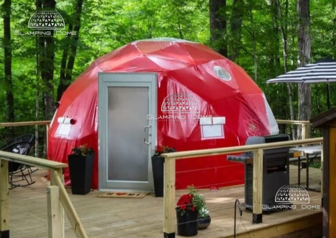 16.4-foot (5-meter) geodesic dome tent, sold by Glamping Dome Store, featuring a vibrant red PVC weather-resistant cover, set on a wooden deck in a forest environment at Little Red Homestead, a bed & breakfast in Lake Ann, Michigan, USA. Ideal for glamping sites, outdoor accommodations, or eco-friendly camping experiences. Features a sturdy entrance door, panoramic window, and ventilation options for all-season use.