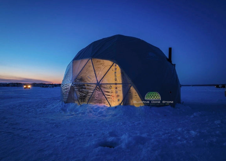 Geodesic dome tent with a grey PVC cover, installed on the frozen surface of Sylvan Lake, Alberta, Canada, as a Glamping Dome Store project. This 19.7-foot (6-meter) dome was designed as an Airbnb fishing shack, featuring a transparent panoramic window. Warm interior lighting contrasts with the icy blue surroundings, creating a unique and cozy retreat for ice fishing enthusiasts.